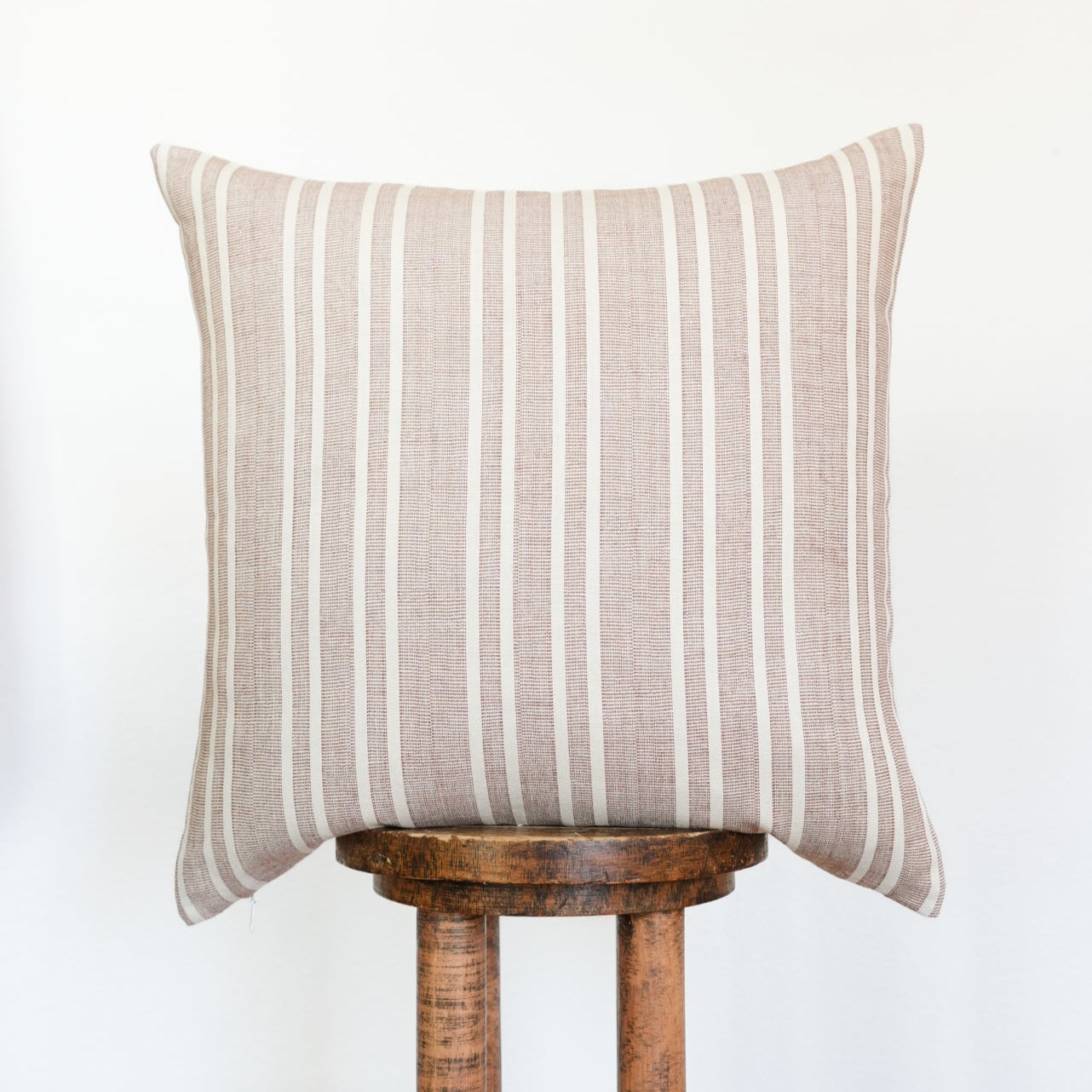 Striped pillow on a wooden stool against a white background